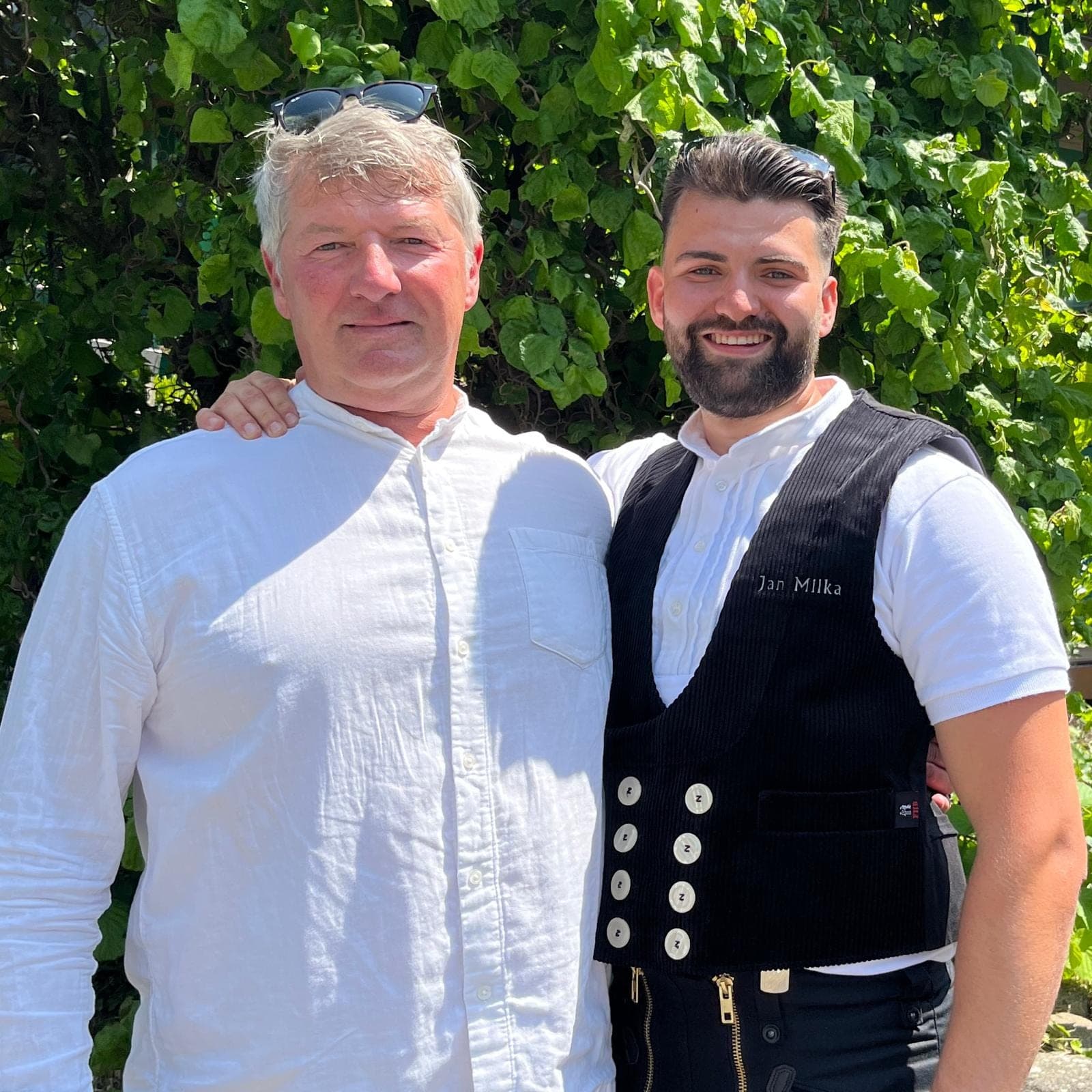 Jörg und Jan Milka stehen nebeneinander vor einer grünen Hecke, Jan in der schwarzen Zunftweste mit dem Namen „Jan Milka“